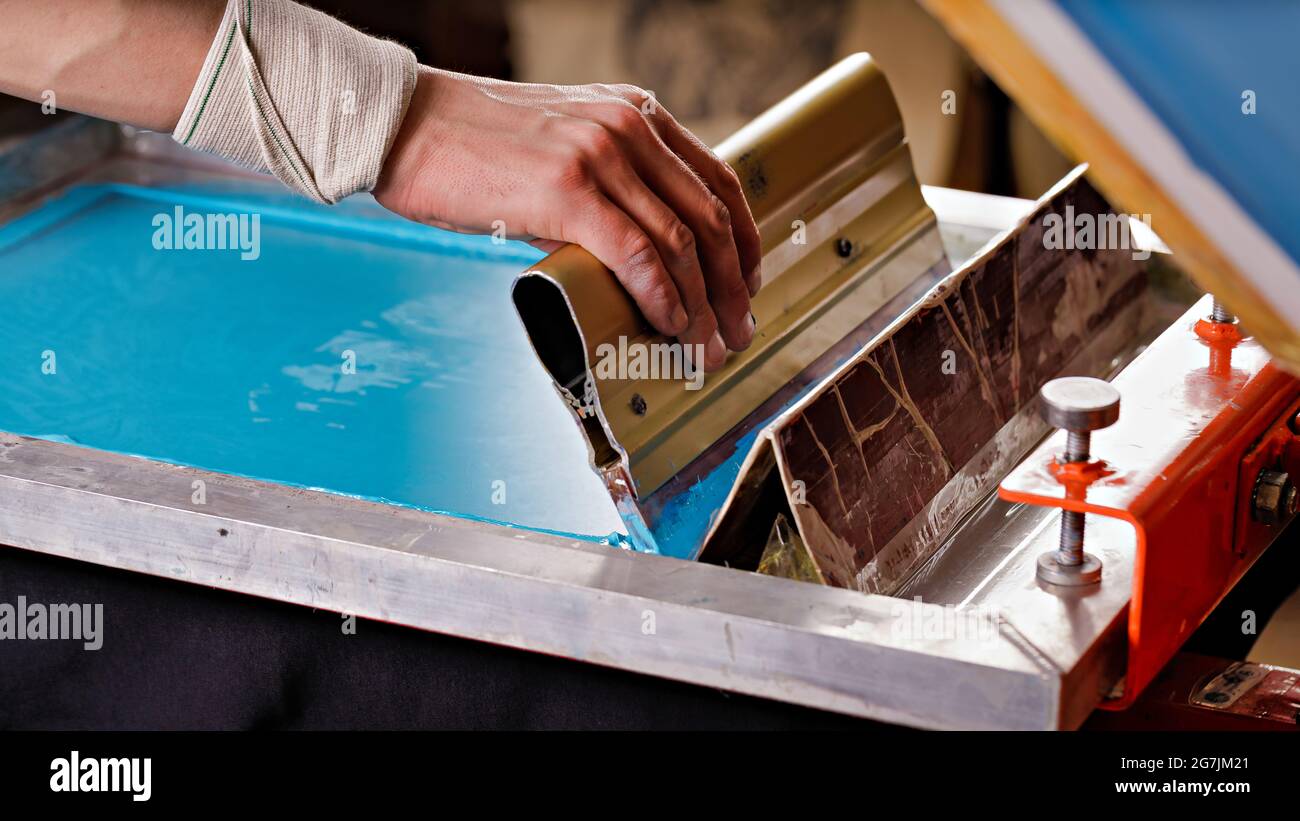 selective focus photo of male hand with a squeegee. serigraphy production. printing images on clothes by silk screen method in a design studio Stock Photo