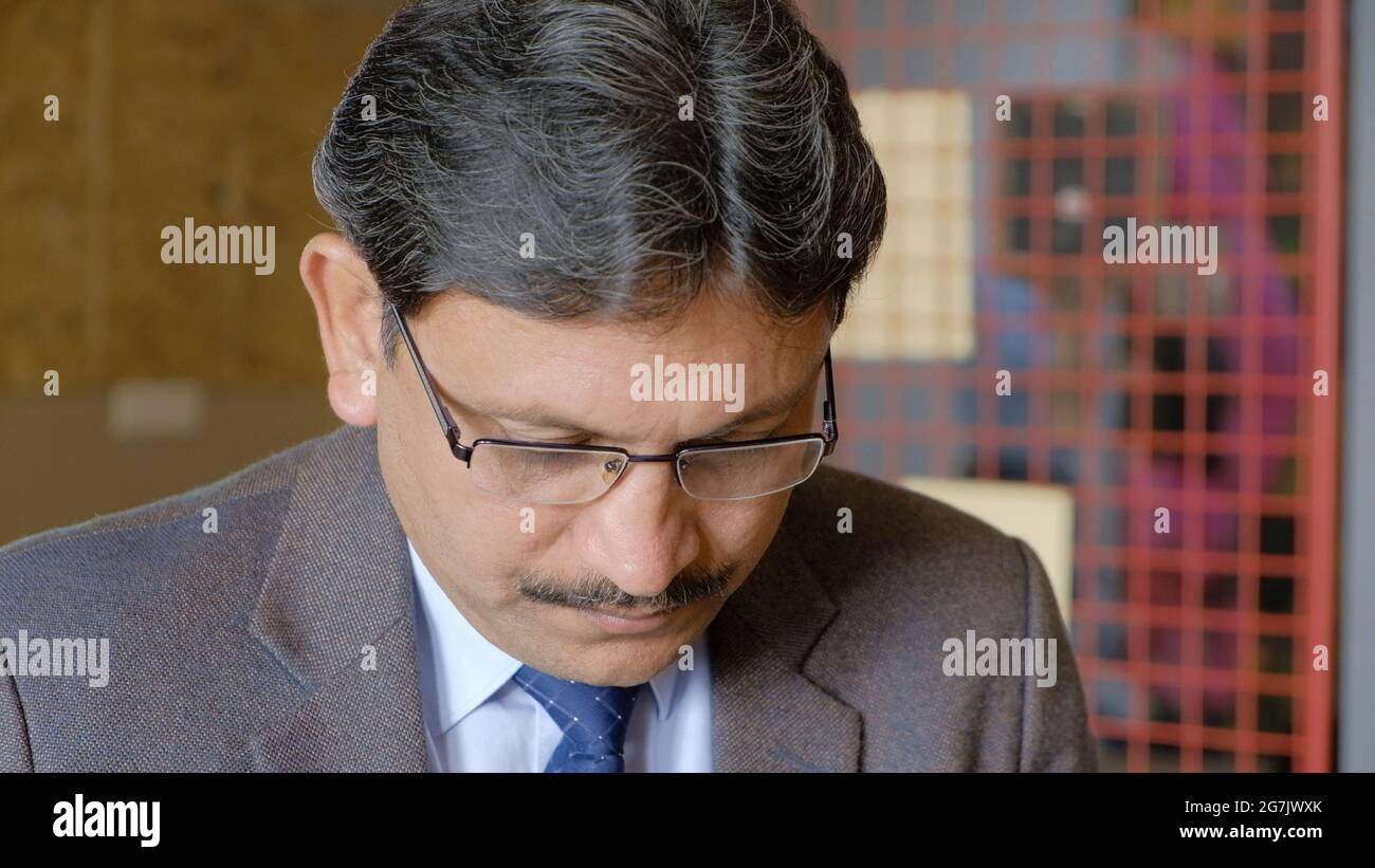 Closeup shot of a South Asian male in a suit with looking at something with head down Stock Photo