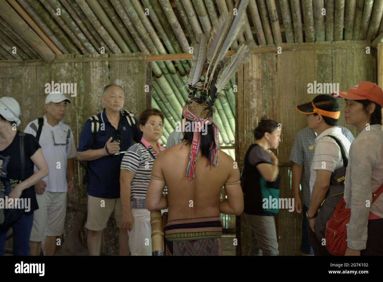 A tourism worker wearing indigenous attire is giving explanations to tourists at Mari Mari Cultural Village, a village that is designed to showcase the cultures of five ethnic groups of Sabah—a Malaysian state in North Borneo, which is located on the outskirts of Kota Kinabalu in Sabah, Malaysia. Stock Photo