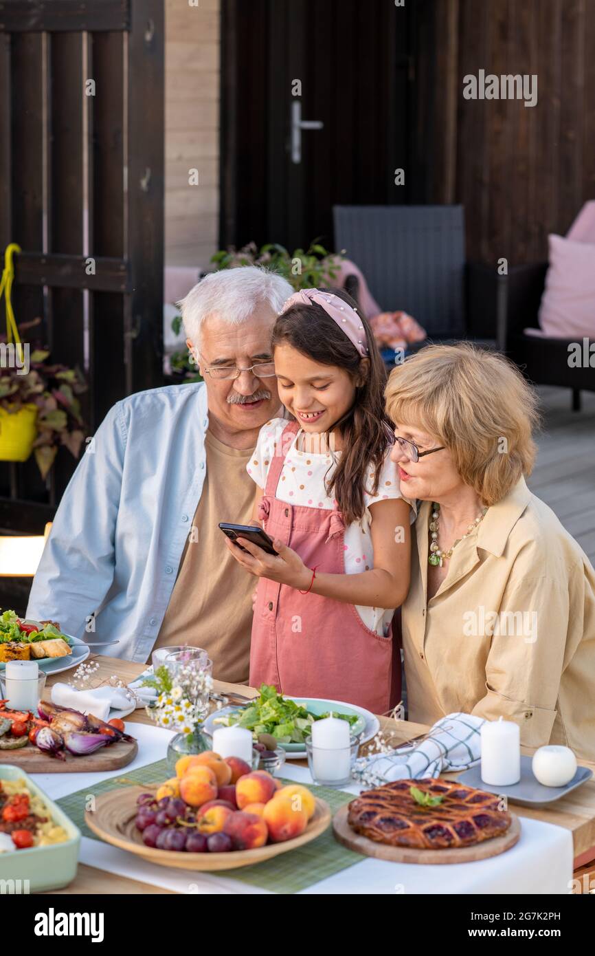 Adorable little girl showing application on tablet computer to her grandfather and grandmother at dinner table Stock Photo