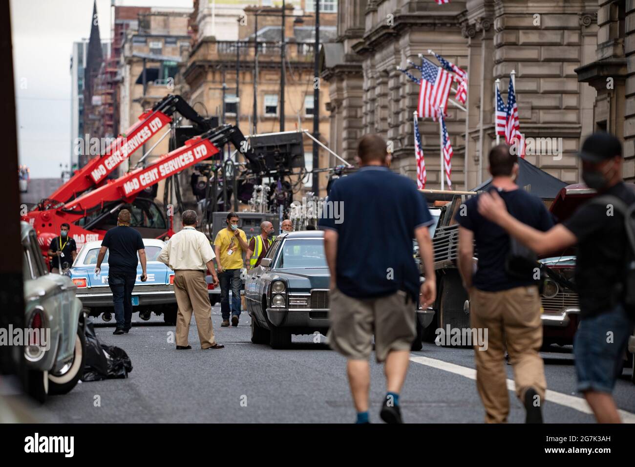 Glasgow, Scotland, UK. 14th July, 2021. PICTURED: Day 2 of filming of Hollywood blockbuster movie of Indiana Jones 5. Police cars, yellow taxi cabs and the presidential car are in the street. The centre of Glasgow city centre has been turned into a 1960s New York City scene, with masses of American flags and stars and stripes bunting hanging from the buildings, shop fronts and signage which include the street furniture and lamp posts resembling the era. Credit: Colin Fisher/Alamy Live News Stock Photo