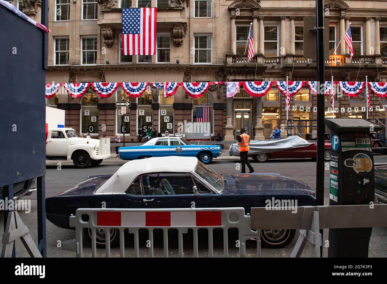 Glasgow, Scotland, UK. 14th July, 2021. PICTURED: Day 2 of filming of Hollywood blockbuster movie of Indiana Jones 5. Police cars, yellow taxi cabs and the presidential car are in the street. The centre of Glasgow city centre has been turned into a 1960s New York City scene, with masses of American flags and stars and stripes bunting hanging from the buildings, shop fronts and signage which include the street furniture and lamp posts resembling the era. Credit: Colin Fisher/Alamy Live News Stock Photo