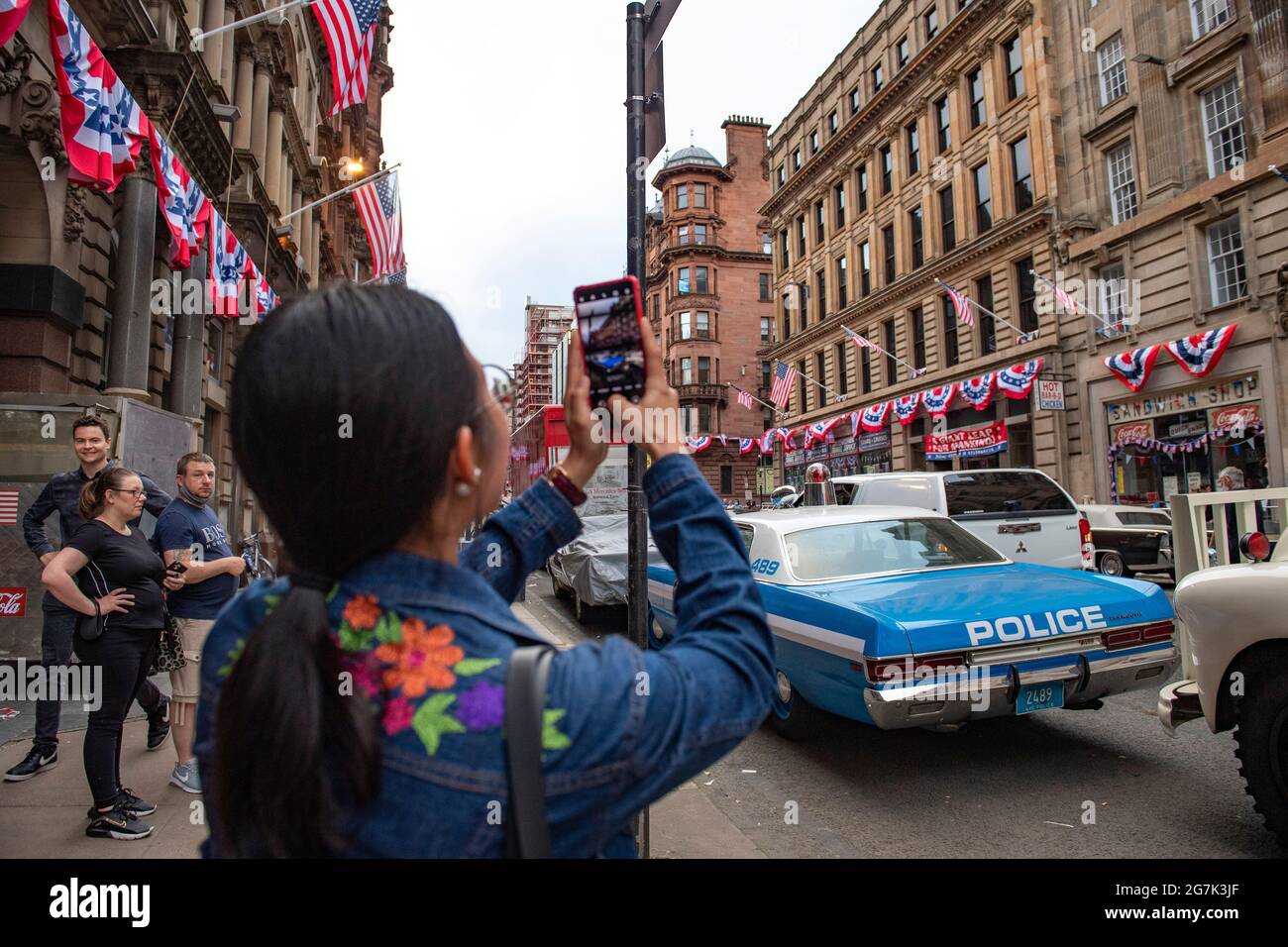 Glasgow, Scotland, UK. 14th July, 2021. PICTURED: Day 2 of filming of Hollywood blockbuster movie of Indiana Jones 5. Police cars, yellow taxi cabs and the presidential car are in the street. The centre of Glasgow city centre has been turned into a 1960s New York City scene, with masses of American flags and stars and stripes bunting hanging from the buildings, shop fronts and signage which include the street furniture and lamp posts resembling the era. Credit: Colin Fisher/Alamy Live News Stock Photo