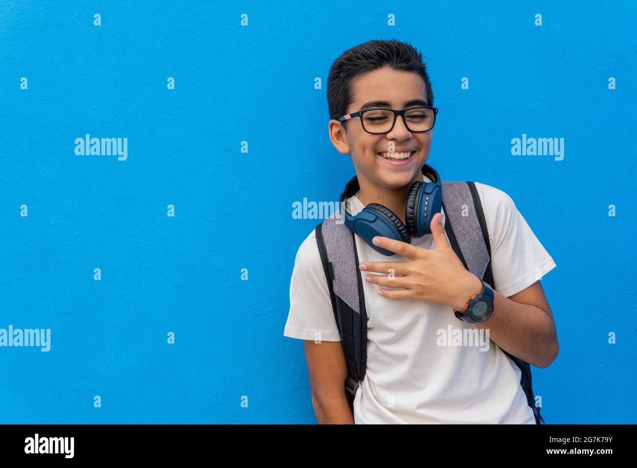 Portrait of a boy with glasses and backpack in front of a blue wall ...