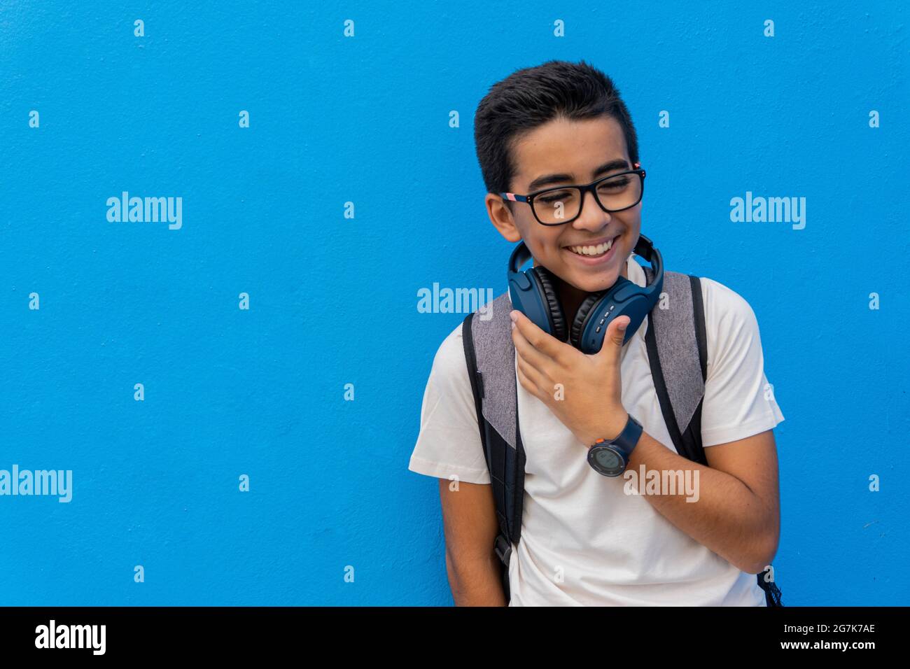 Portrait of a boy with glasses and backpack in front of a blue wall ...