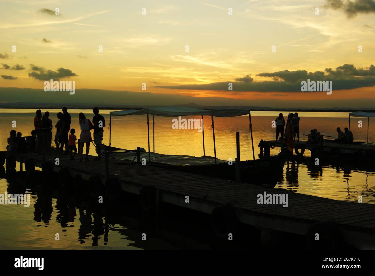 Silhouettes of tourists on a pier and in boats on the sea during a ...