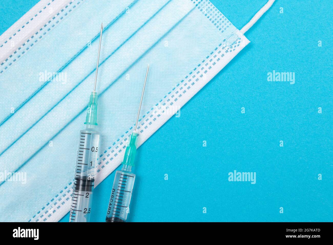 Several Syringe and Face Mask on Blue Table - Top View. Syringes are Prepared for Vaccination or Injection. Medical Experiment. Blue Disposable Medical Mask. Virus protection - Flat Lay Stock Photo