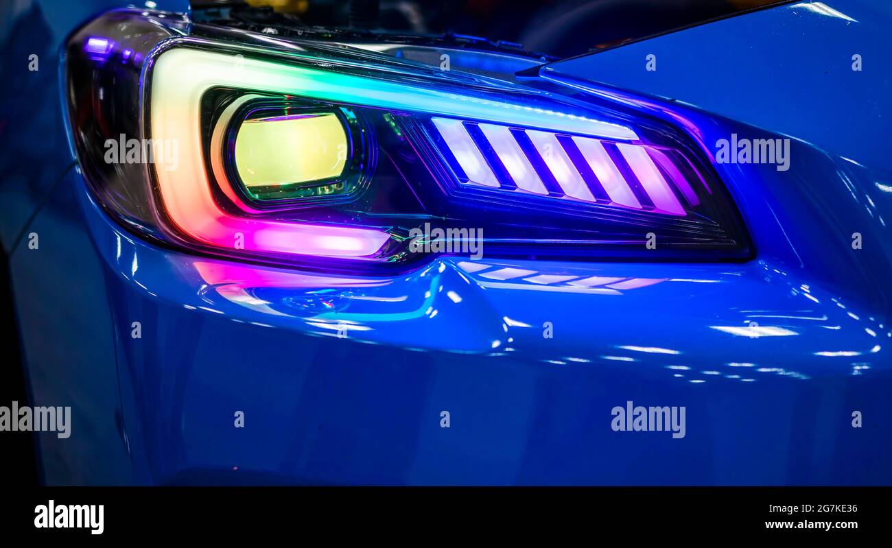 Fragment of the turned on glass headlight of the blue shiny car with neon  spectrum of light reflection and glare of surrounding objects on the  combine Stock Photo - Alamy