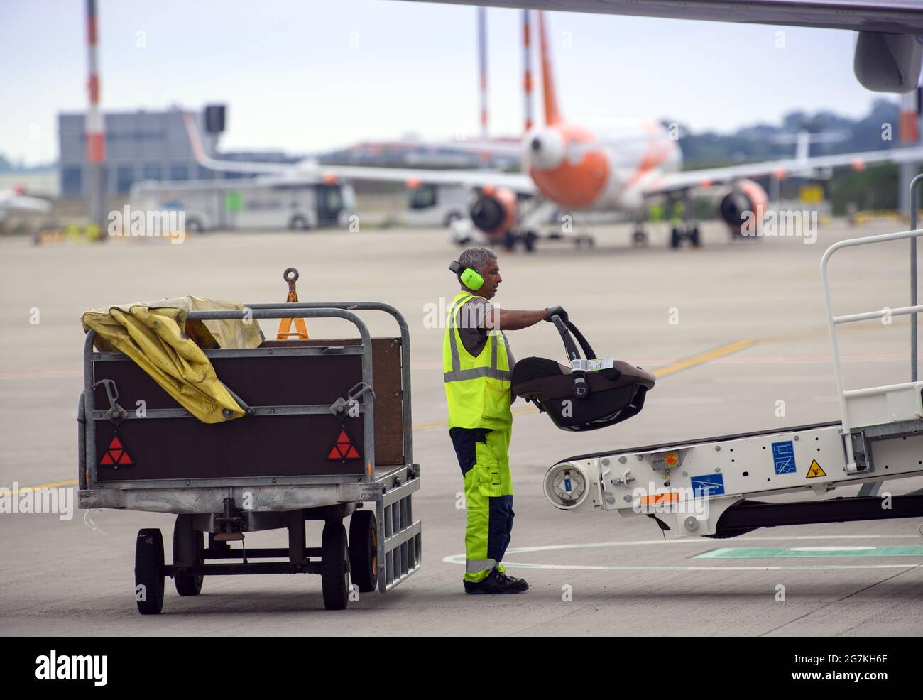 14 July 2021, Brandenburg, Schönefeld: A WISAG Aviation employee loads a child's seat onto the baggage conveyor belt (power stow) on the aircraft on the apron of BER 'Willy Brandt' Airport. During the E-Day, the ground handling service provider presented the Smart Trainer, a ground power unit for supplying power to aircraft waiting at outside positions, and the emission-free handling of an aircraft. The project 'WISAG - Ready for Green' contributes to the reduction of CO2 emissions and thus makes flying more environmentally friendly. Photo: Soeren Stache/dpa-Zentralbild/dpa Stock Photo