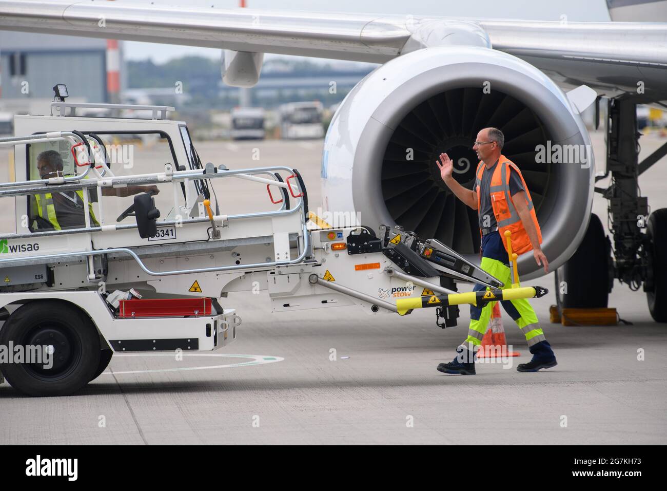 14 July 2021, Brandenburg, Schönefeld: A WISAG Aviation employee directs a baggage conveyor belt (power stow) away from the aircraft on the apron of BER 'Willy Brandt' Airport. During the E-Day, the ground handling service provider presented the Smart Trainer, a ground power unit for supplying power to aircraft waiting at external positions, and the emission-free handling of an aircraft. The project 'WISAG - Ready for Green' contributes to the reduction of CO2 emissions and thus makes flying more environmentally friendly. Photo: Soeren Stache/dpa-Zentralbild/dpa Stock Photo