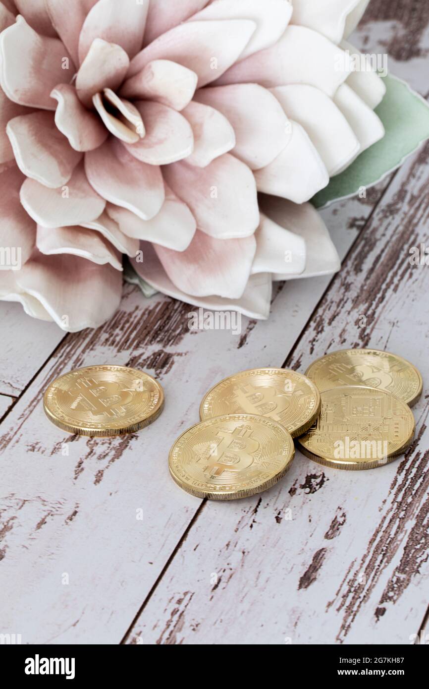 Small round shape golden bit coins tokens in front of a big flower with pink petals in the background and a white wooden surface Stock Photo