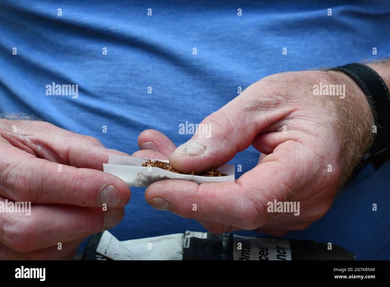 A man using tobacco and white papers to roll a rollup cigarette Stock