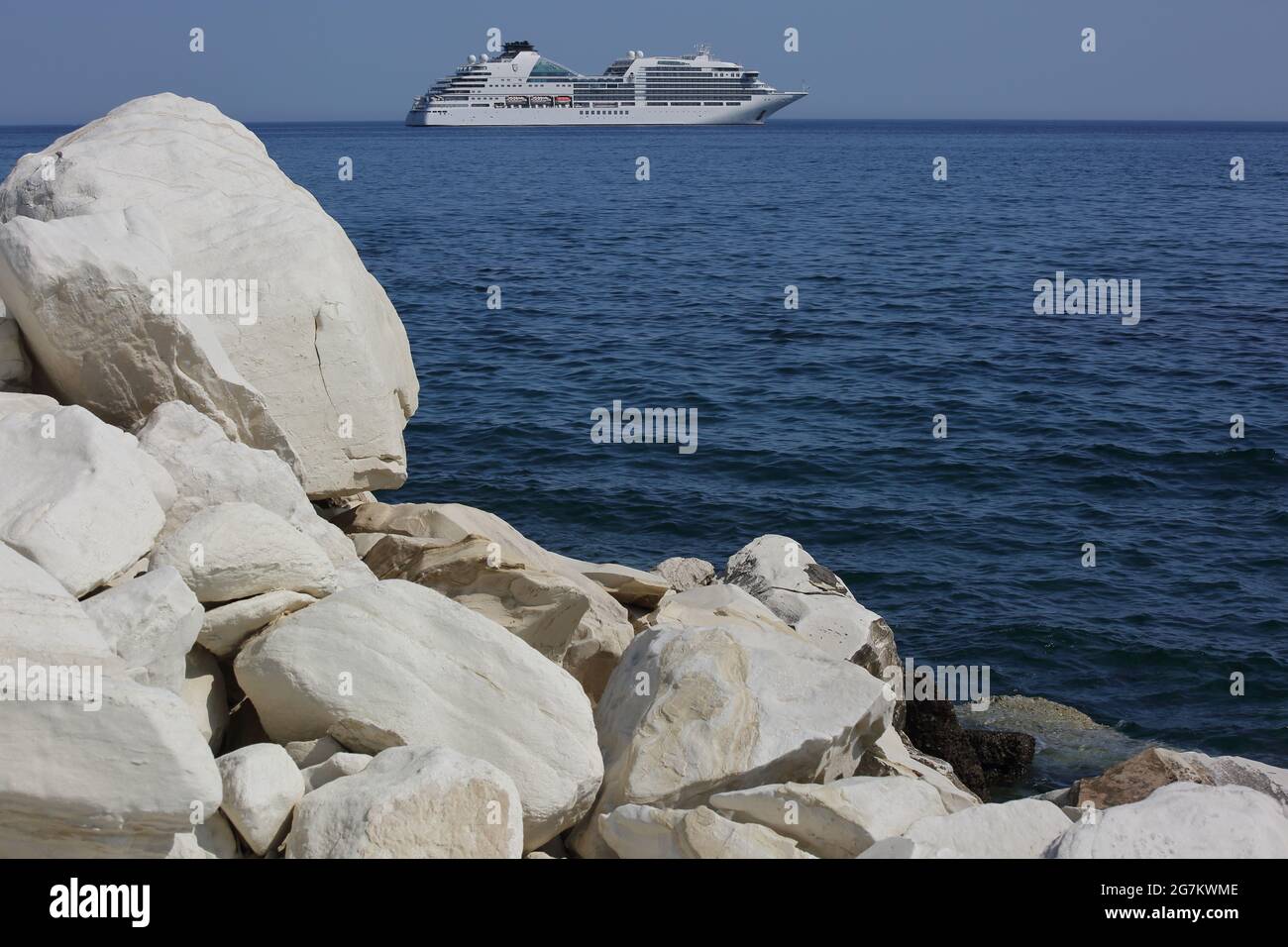 Luxury cruise boat on the Mediterranean sea seen on horizon, rocky coast in foreground Stock Photo