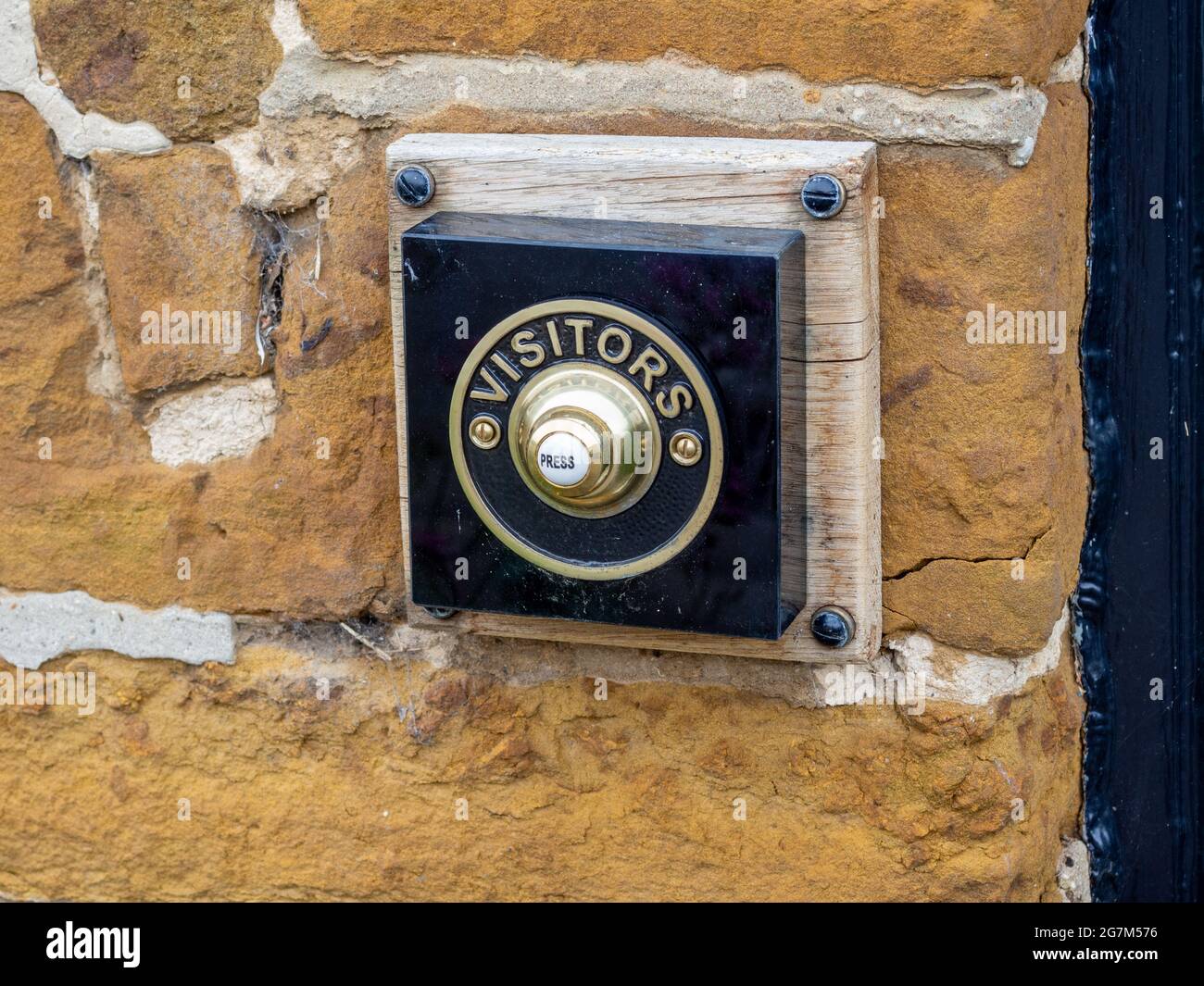 Traditional brass bell push, marked Visitors, set into an old stone building, UK Stock Photo