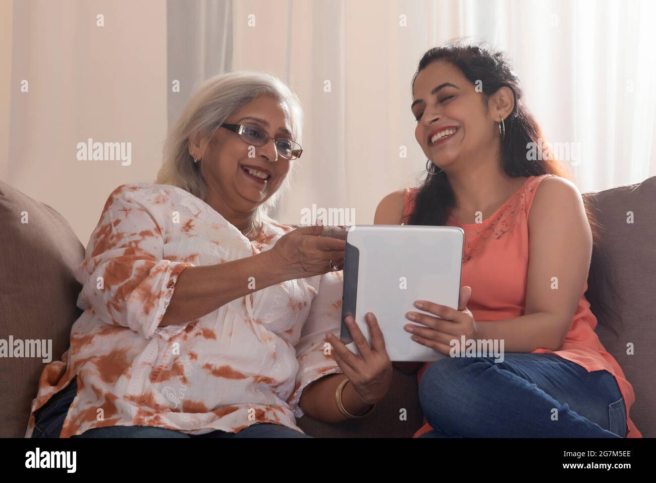 A DAUGHTER AND MOTHER USING A TABLET TO VIDEO CALL LOVED ONES Stock Photo