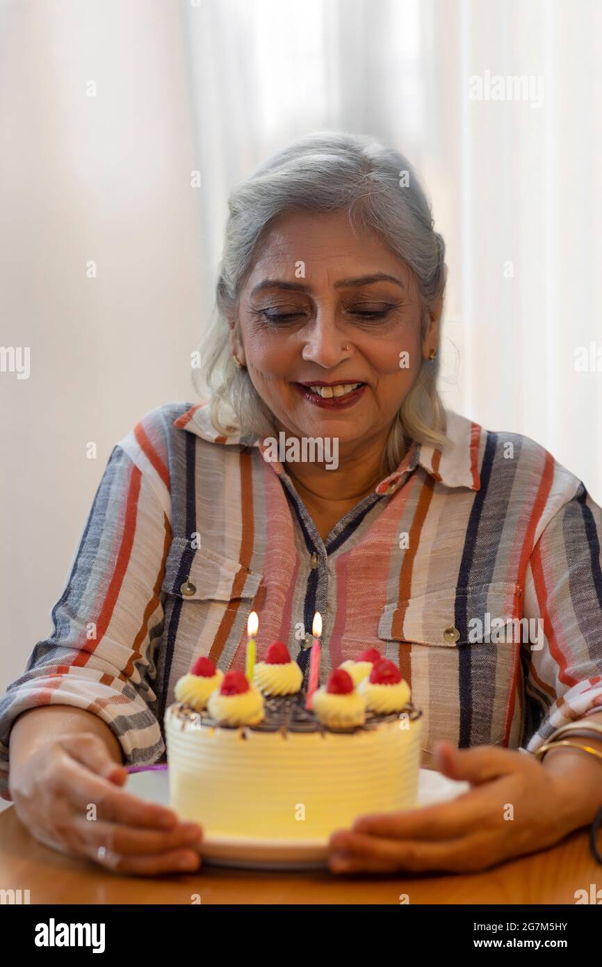 A MATURE ADULT WOMAN SMILING AND LOOKING AT BIRTHDAY CAKE Stock Photo
