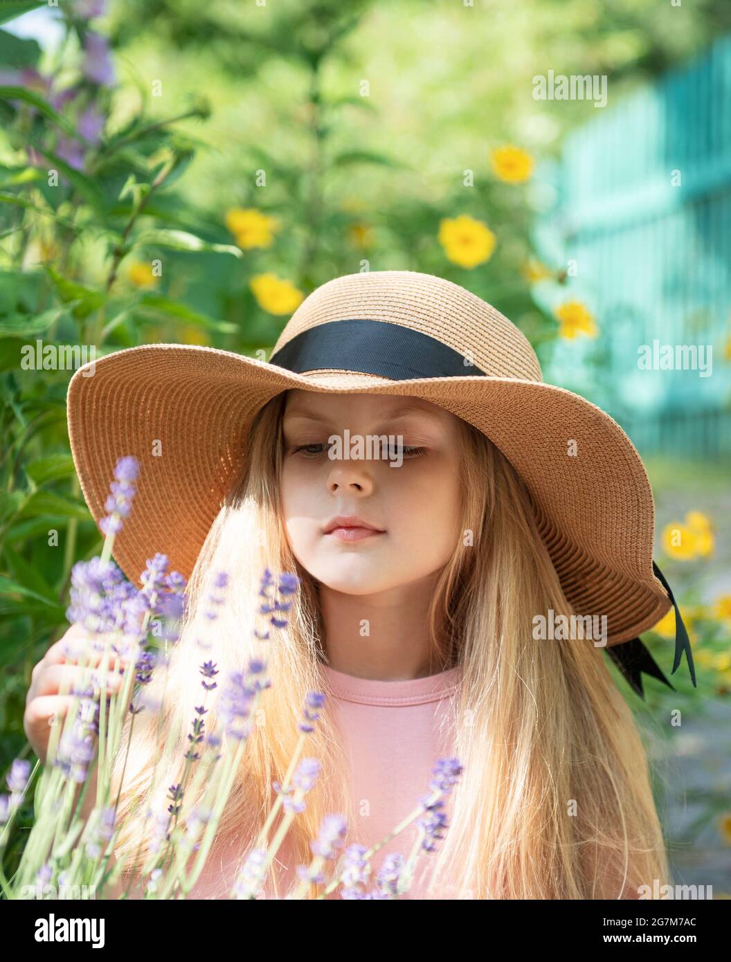 Little girl in a straw hat surrounded by lavender flowers. Portrait of ...