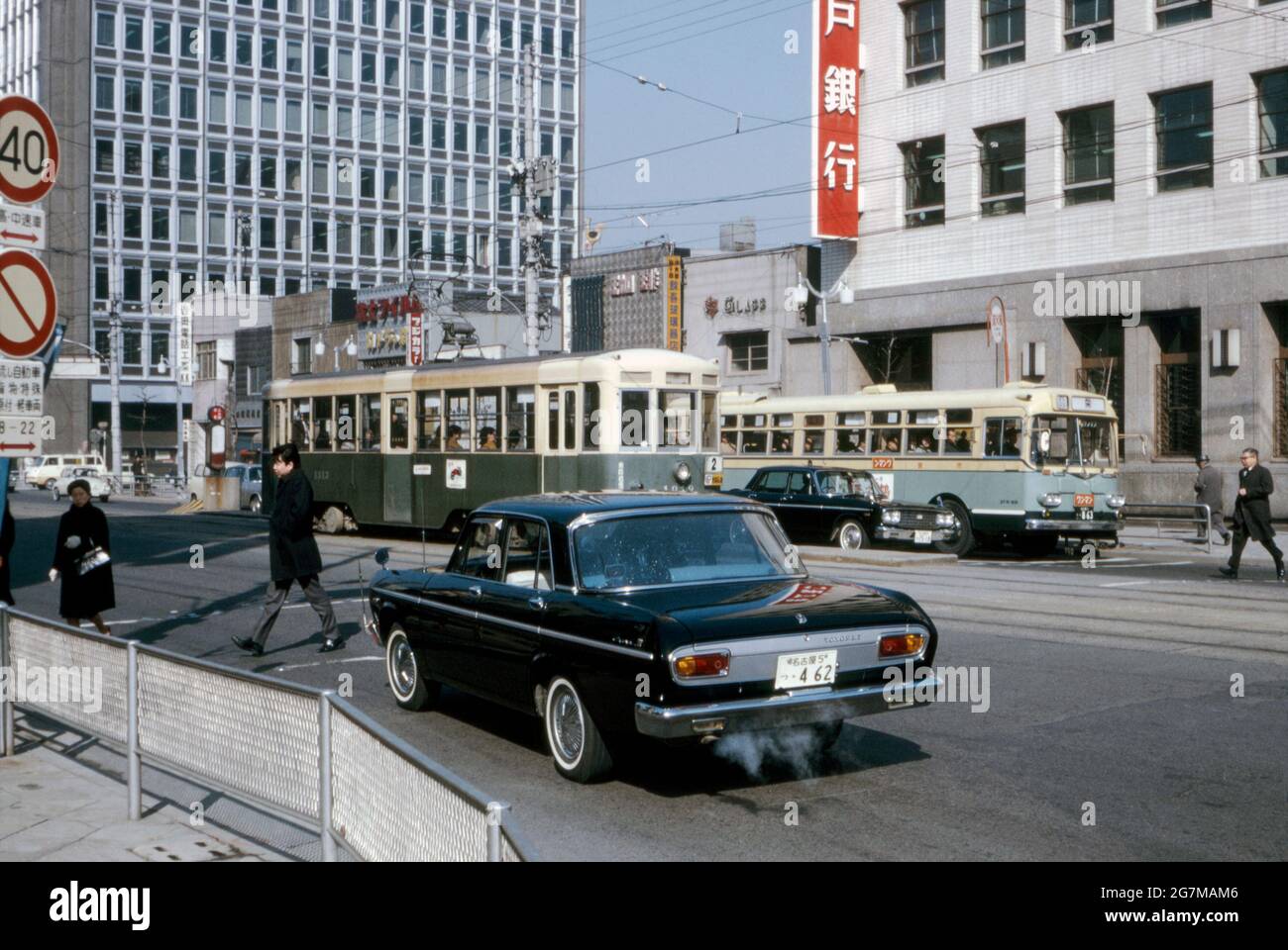 Traffic stopped at a pedestrian crossing in downtown Tokyo, Japan in 1969.  Two forms of public transport are seen – a tram (streetcar number 1813 on  route 2) and a bus. One