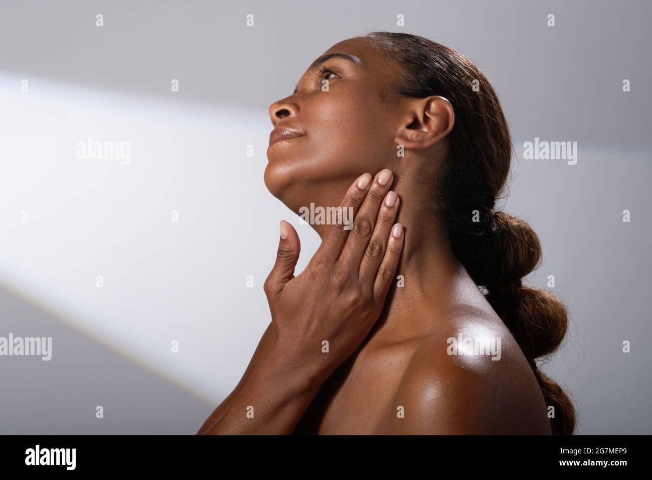 Beauty images of a woman with darker skin tone. Head and shoulder pictures of calm, happy lady. Massaging in a cream or balm into her skin. Stock Photo