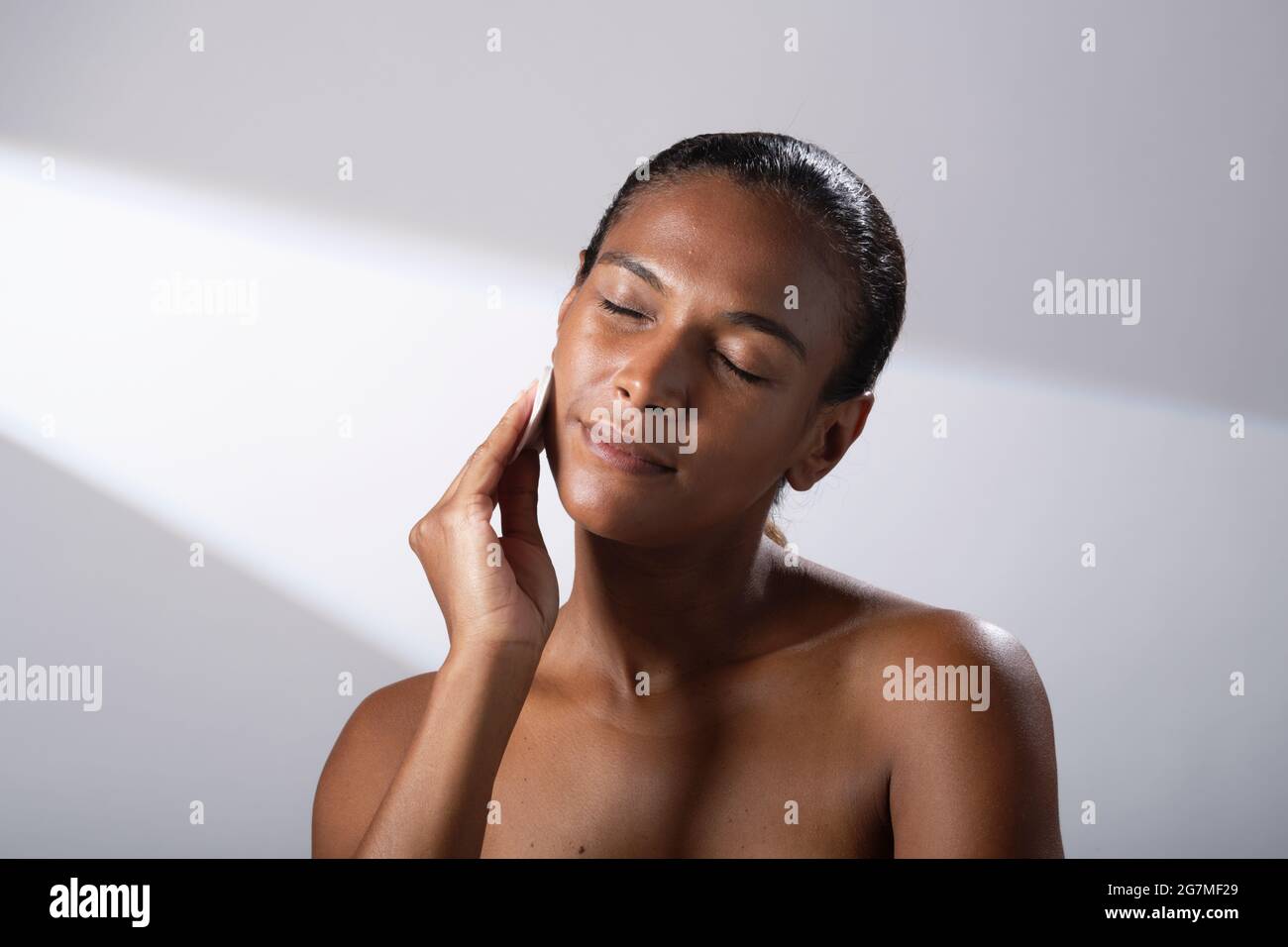 Beauty images of a woman with darker skin tone. Head and shoulder pictures of contented, happy lady using cotton face pads. Stock Photo