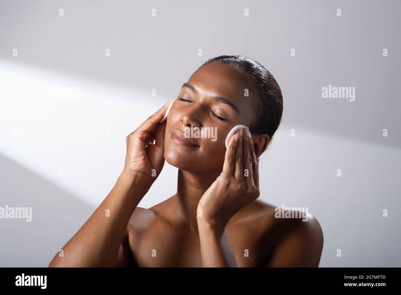 Beauty images of a woman with darker skin tone. Head and shoulder pictures of contented, happy lady using cotton face pads. Stock Photo