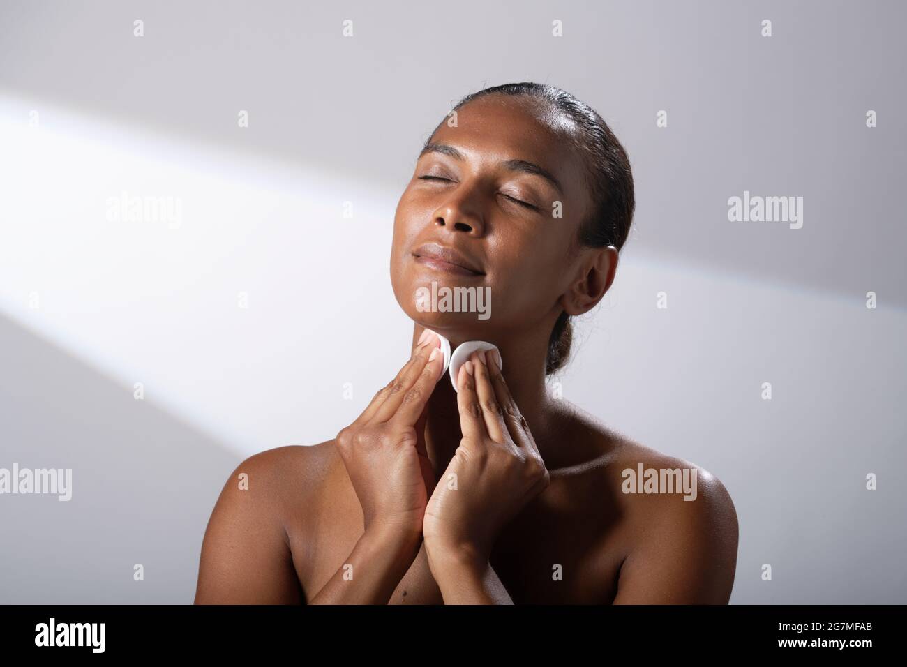 Beauty images of a woman with darker skin tone. Head and shoulder pictures of contented, happy lady using cotton face pads. Stock Photo