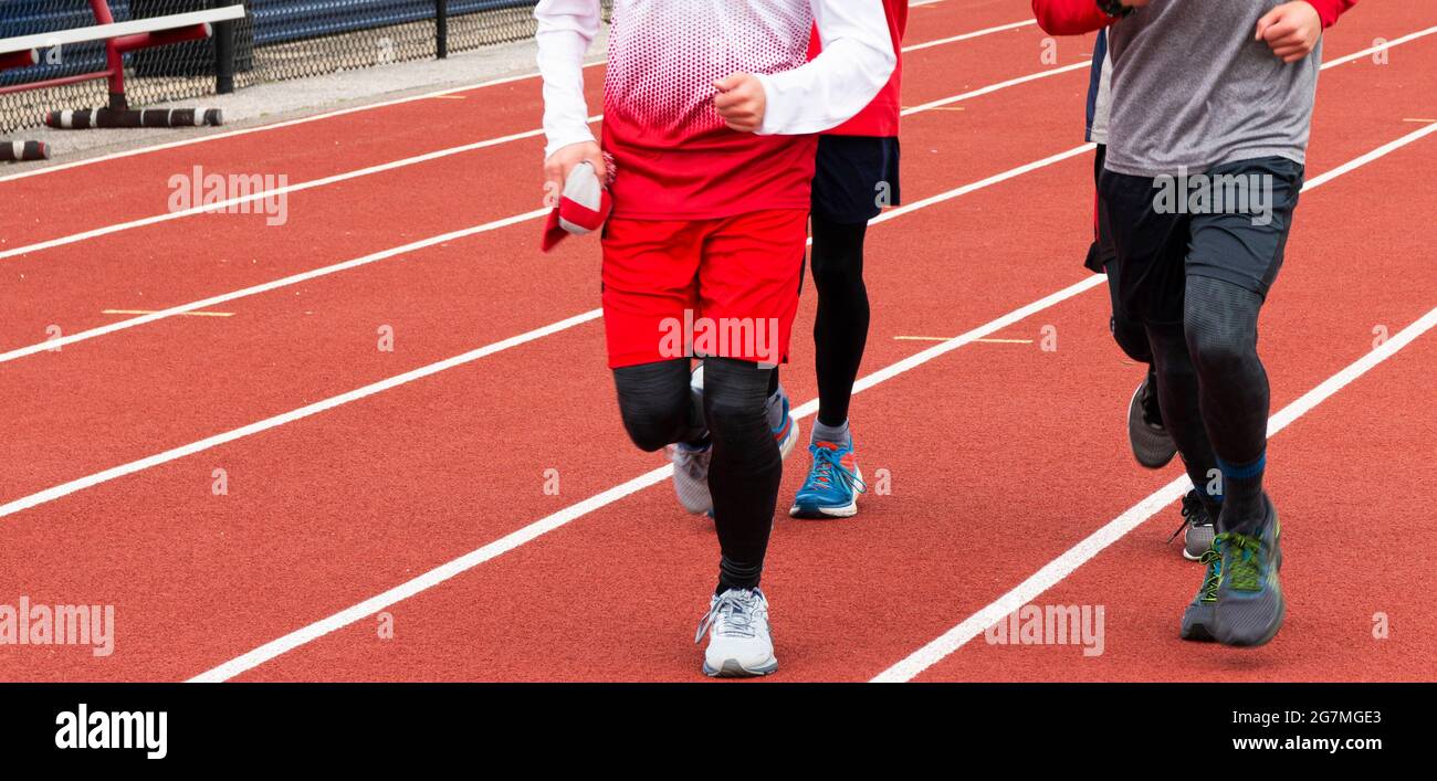 High school boys running laps on a red track during practice on a cold