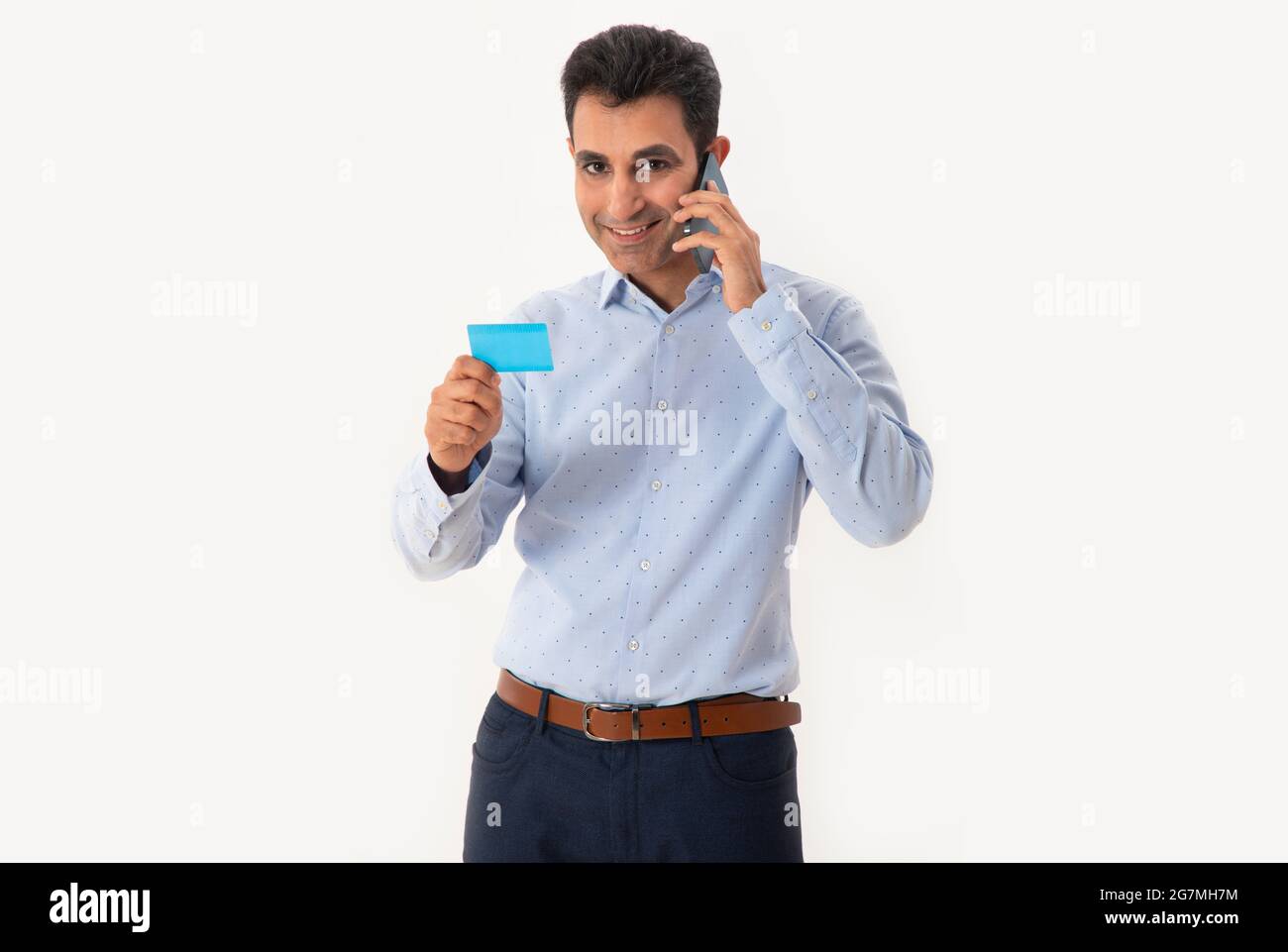 A HAPPY PROFESSIONAL LOOKING AT CAMERA WHILE HOLDING VISITING CARD AND TALKING ON MOBILE Stock Photo