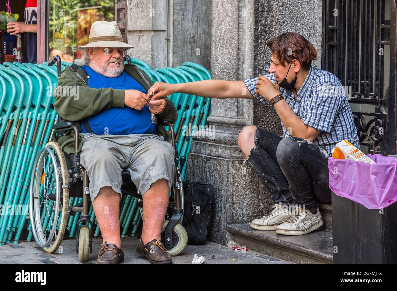 Young man helping older disabled friend roll a cigarette - Saint Gilles, Brussels, Belgium. Stock Photo