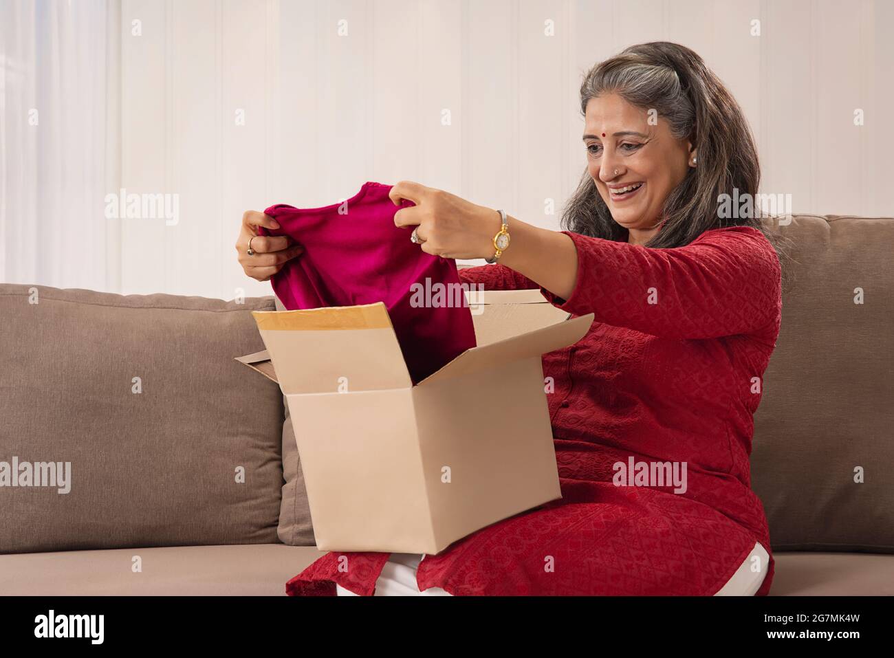 A HAPPY OLD WOMAN LOOKING AT NEW DRESS DELIVERED THROUGH COURIER Stock Photo