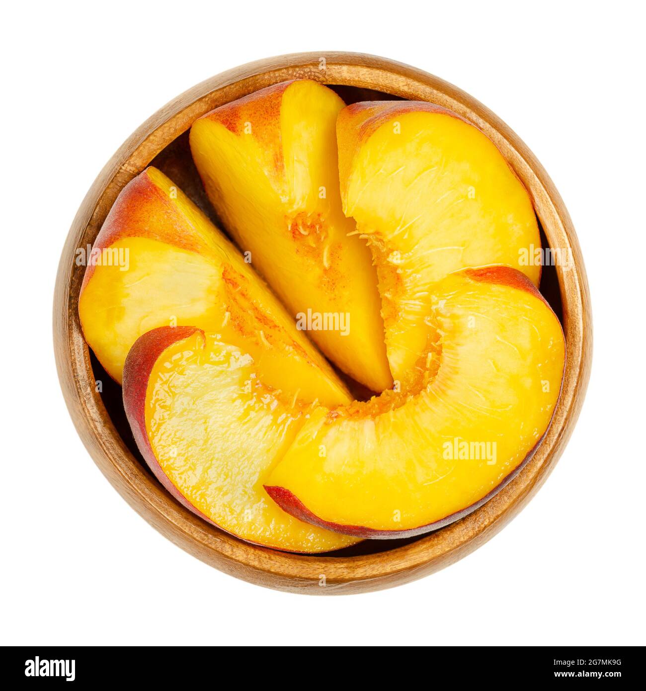 Peach slices in a wooden bowl. Sliced ripe fruit, with a yellow and juicy fruit flesh, and with velvety skin. Prunus persica. Ready to eat. Stock Photo