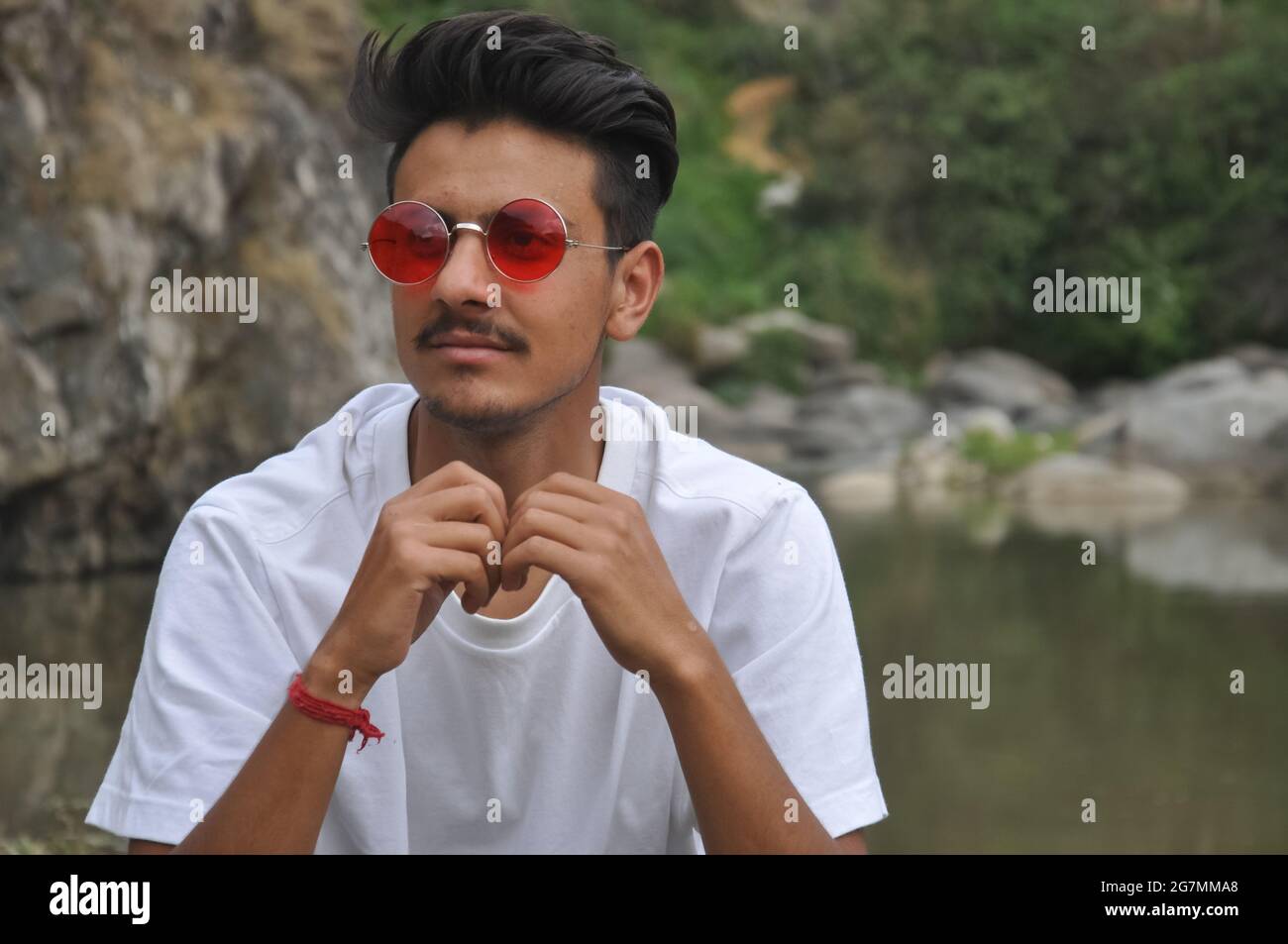 A north Indian young guy sitting beside of river with looking sideways, A guy with wearing white t-shirt and red sunglasses Stock Photo