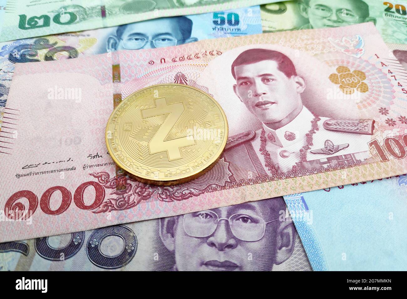 Close-up on a golden Zcash coin on top of a stack of Thai Baht banknotes. Stock Photo