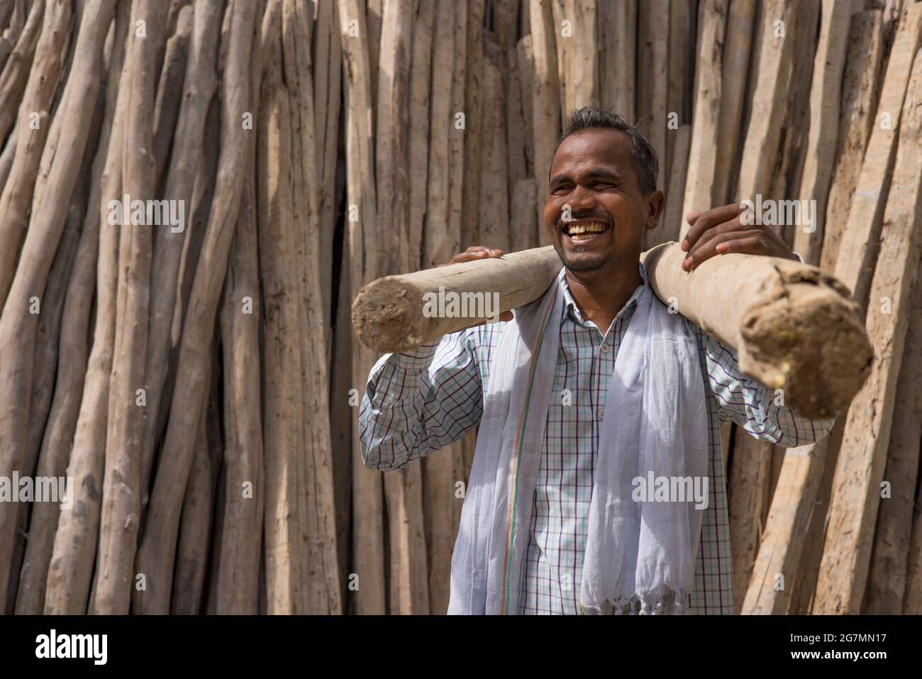 A MANUAL LABOURER CARRYING HEAVY WOODEN POLES LOOKING AWAY AND LAUGHING Stock Photo