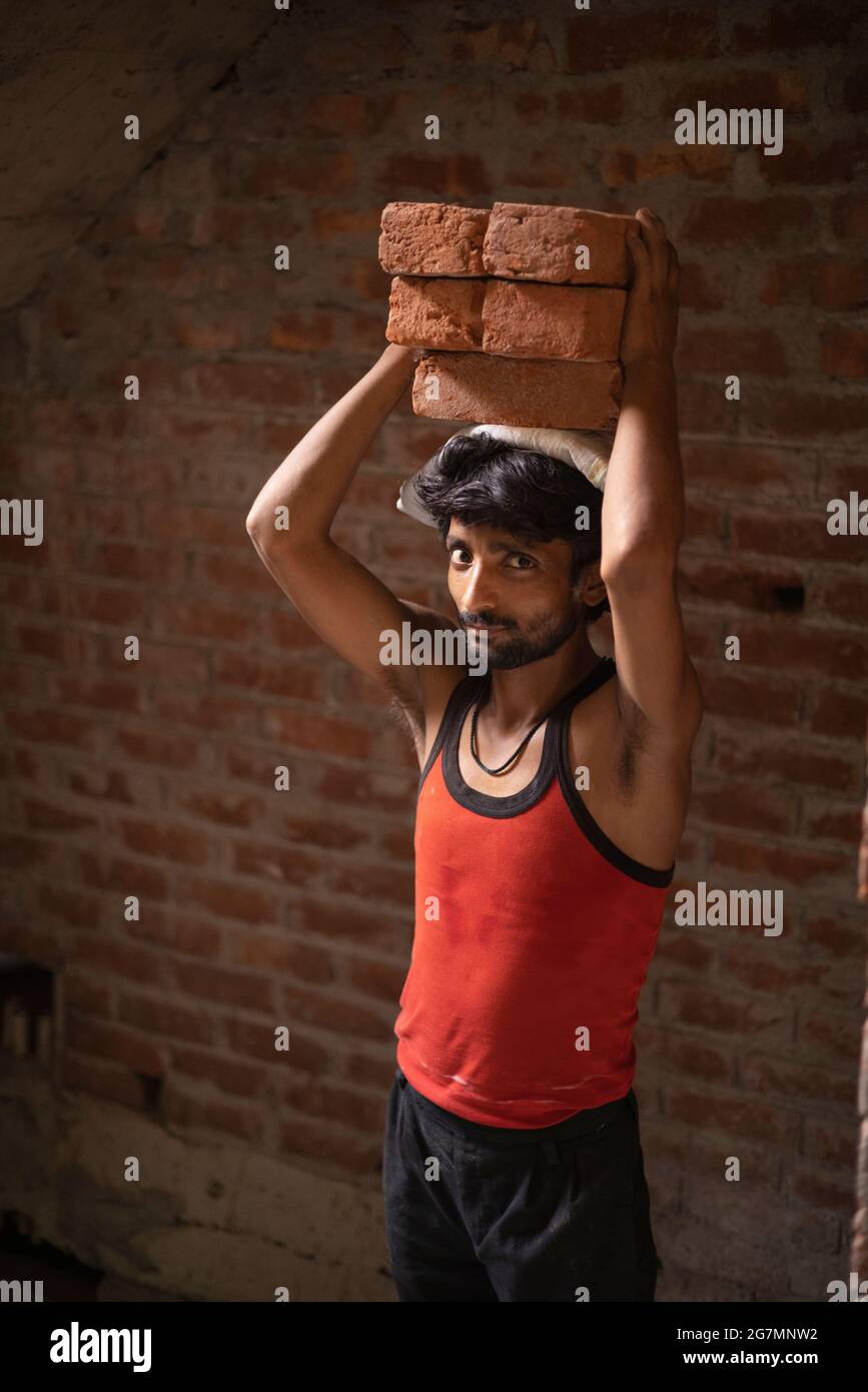 A LABOURER CARRYING BRICKS ON HEAD LOOKING AT CAMERA Stock Photo