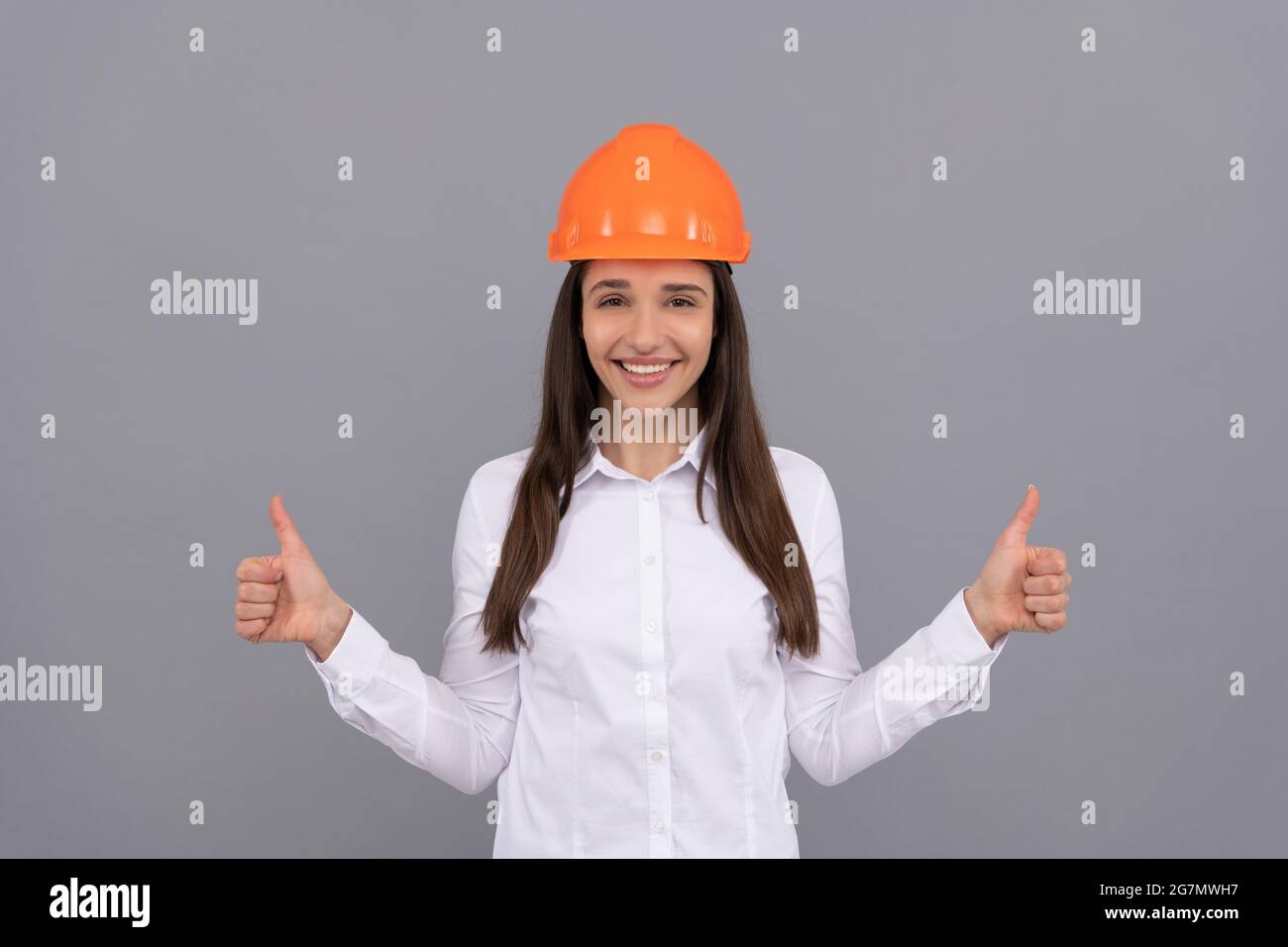 happy woman in protective helmet and white shirt showing thumb up gesture, good result Stock Photo