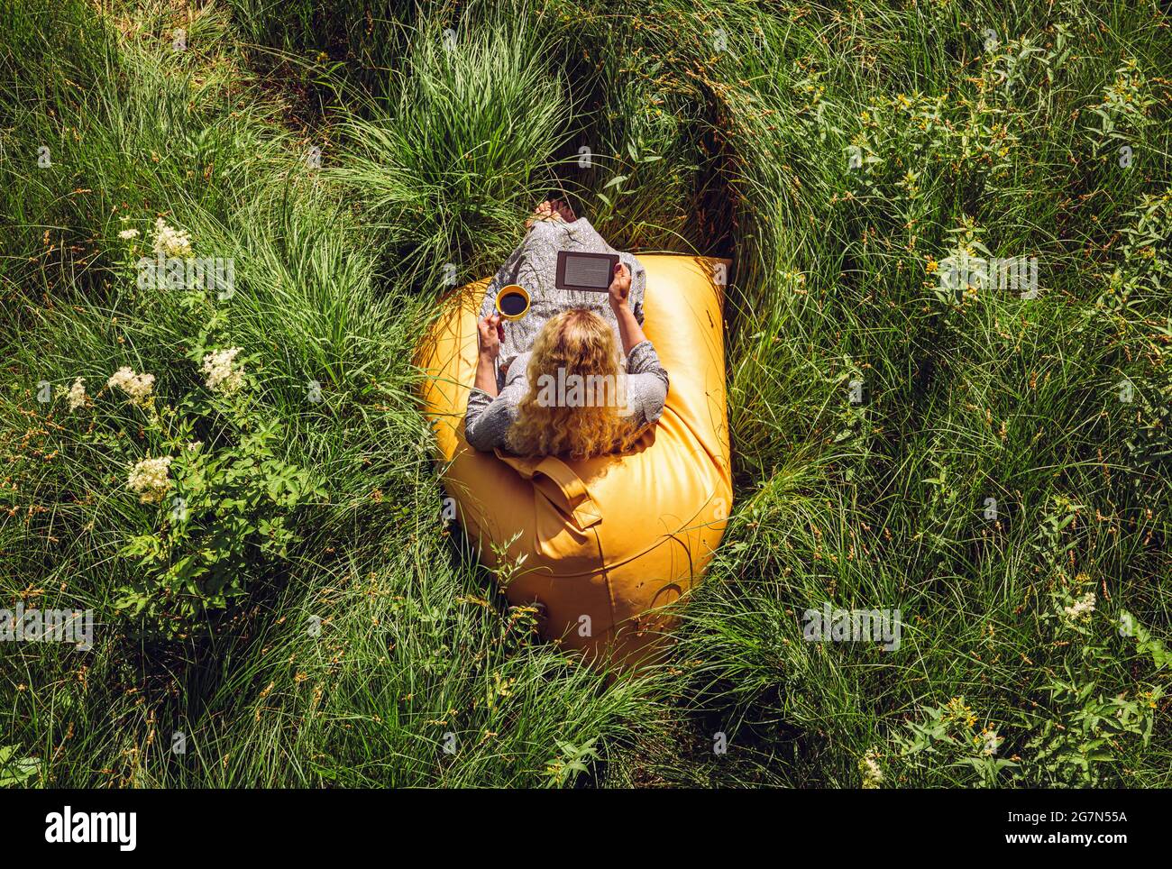 Woman person reading an ebook electronic book and sit on yellow beanbag in wild nature. Above view. Stock Photo