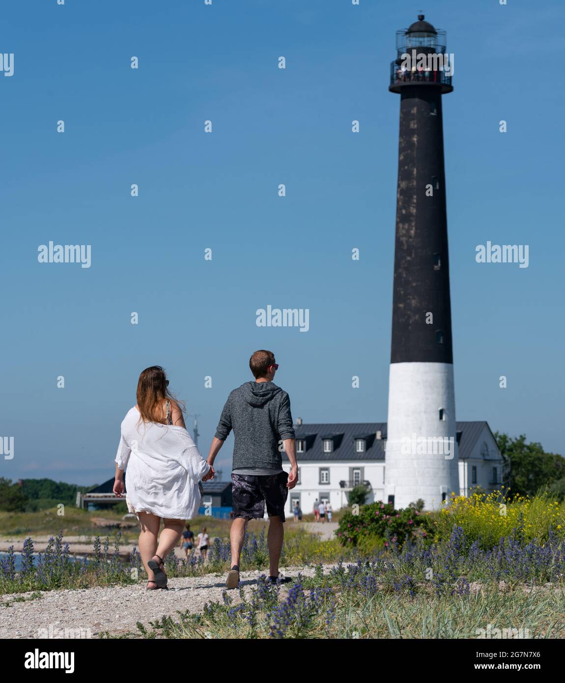Sorvesaar,Estonia-06.21.2021: Lighthouse at the end of Sorve saar peninsula. Tall beacon of light for the ship to guide them. Couple walking up to the tall tower holding hands.  Stock Photo