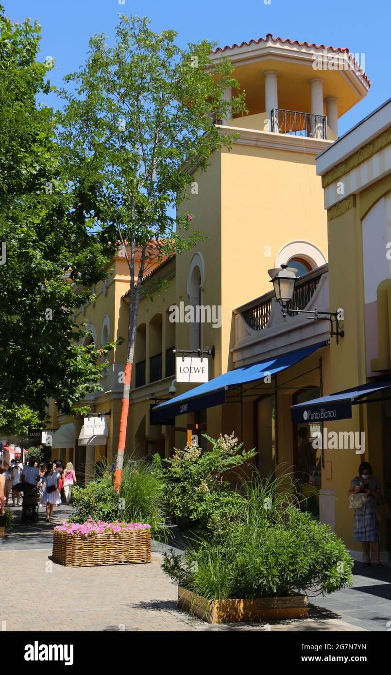Las Rozas outlets shopping mall with signs for Diesel, Asics and Longchamp  with orange banding on tree trunks on a sunny summer afternoon Madrid Spain  Stock Photo - Alamy
