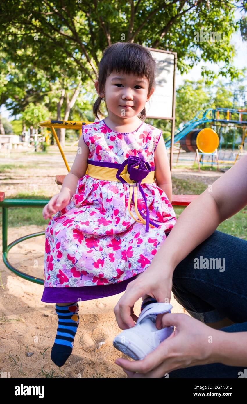 Little asian child, adorable girl in pretty dress on carousel in the park  on summer day. Parent wearing shoes to daughter. Sunlight in the kids  playgr Stock Photo - Alamy