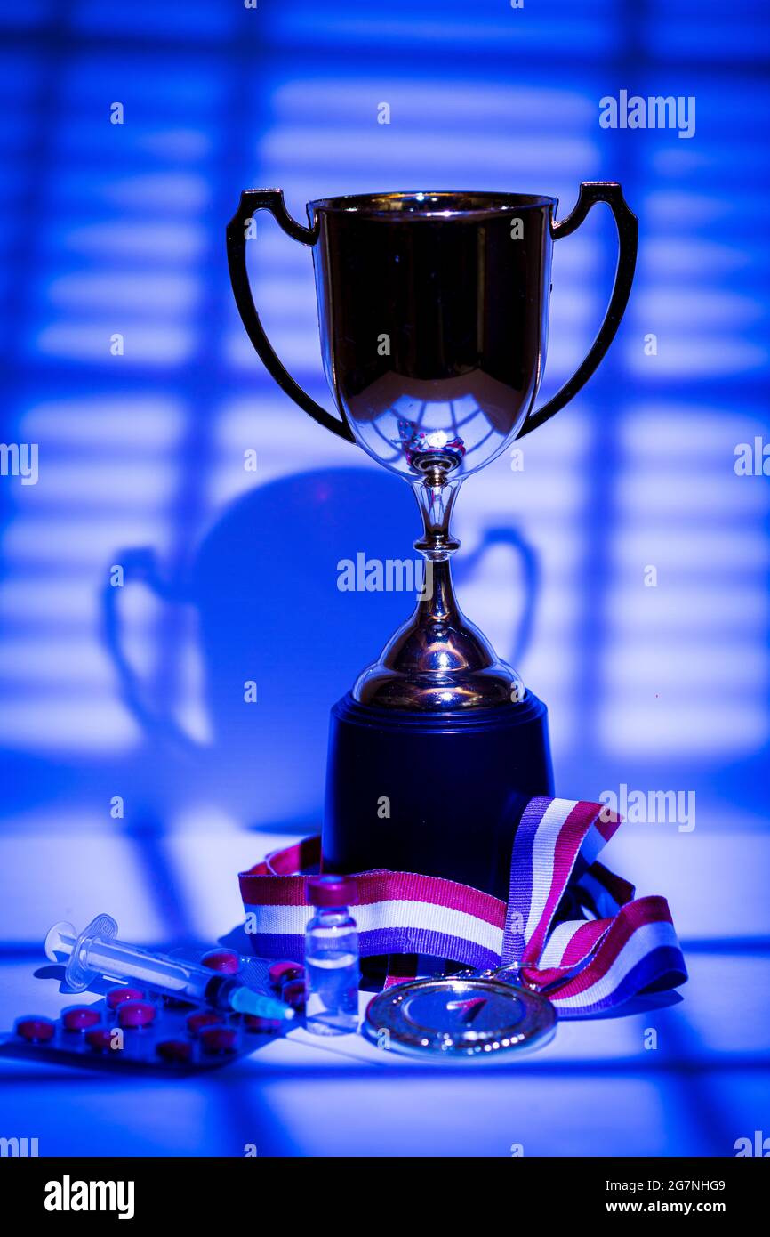 Gold medal and champion's cup, syringe with doping substance, pill tablet  and vial with prohibited substance with lights and shadows of a curtain  ente Stock Photo - Alamy