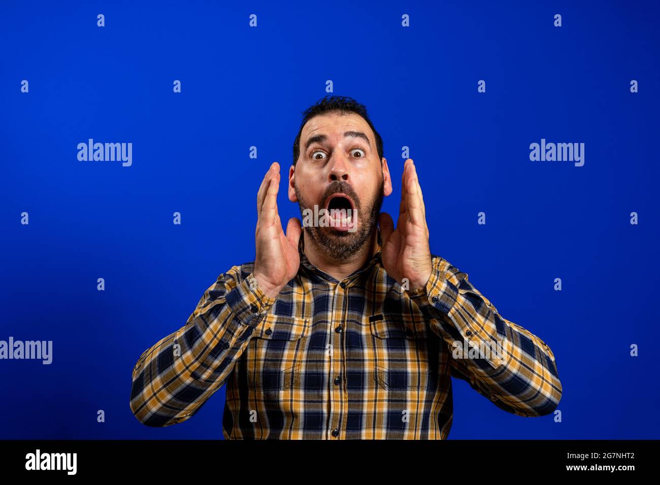 Angry young man yelling screaming. Hipster man with beard in blue plaid checkered shirt Isolated on gray studio Background. Negative face expression Stock Photo