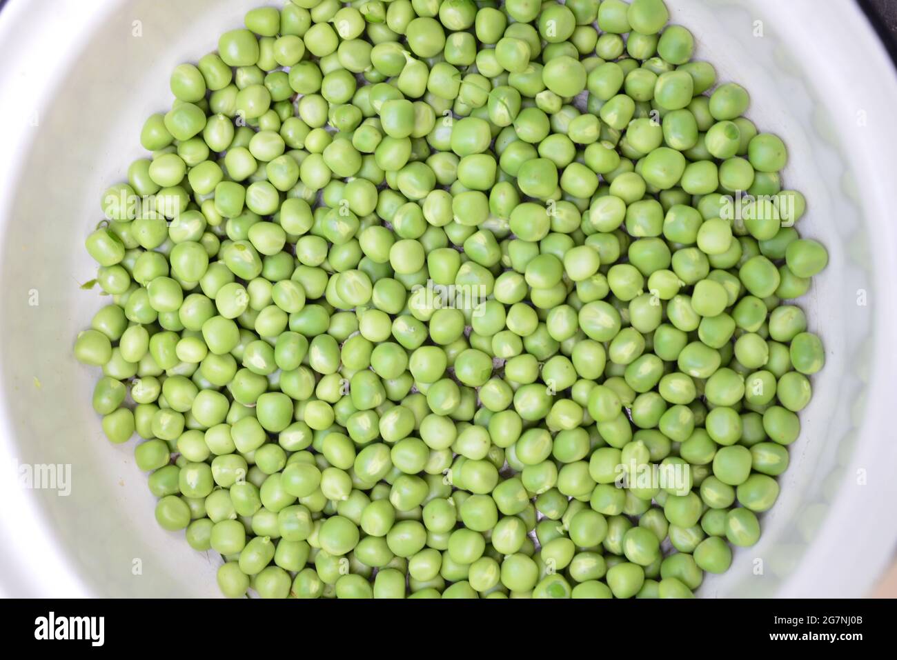 RAW baby peas in small white bowl, on table. Close-up. Stock Photo