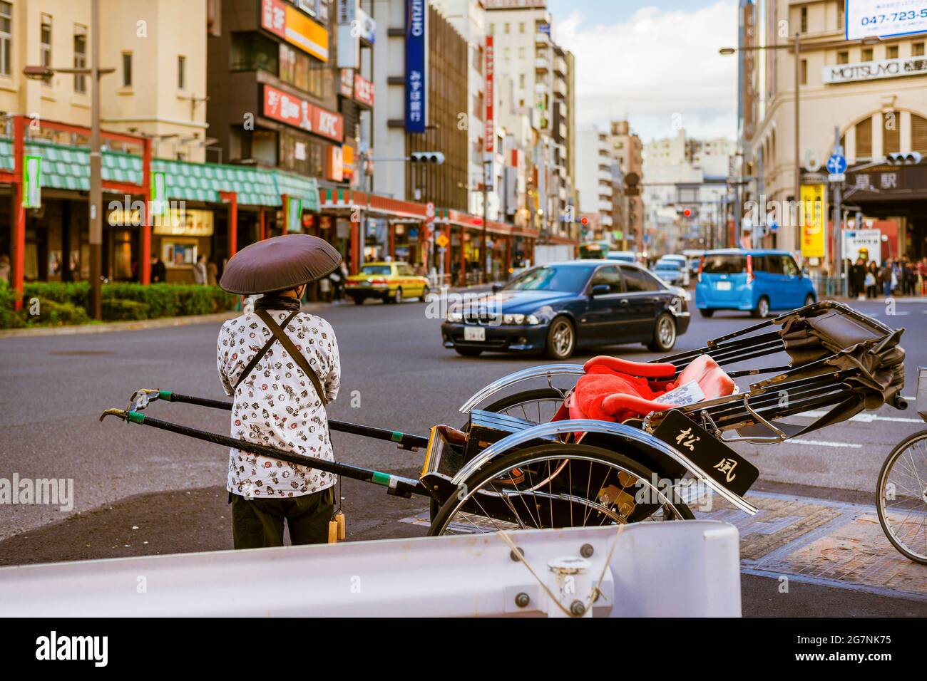 Japan between tradition and modernity. A rickshaw runner looks at the modern cars at Asakusa crossroad in Tokyo Stock Photo