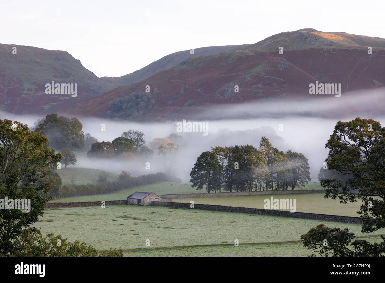 Grasmere, Cumbria, UK, September 29th 2020: Traditional stone barn and walls surrounded by trees and morning mist. Rydal Fell looms in the background. Stock Photo