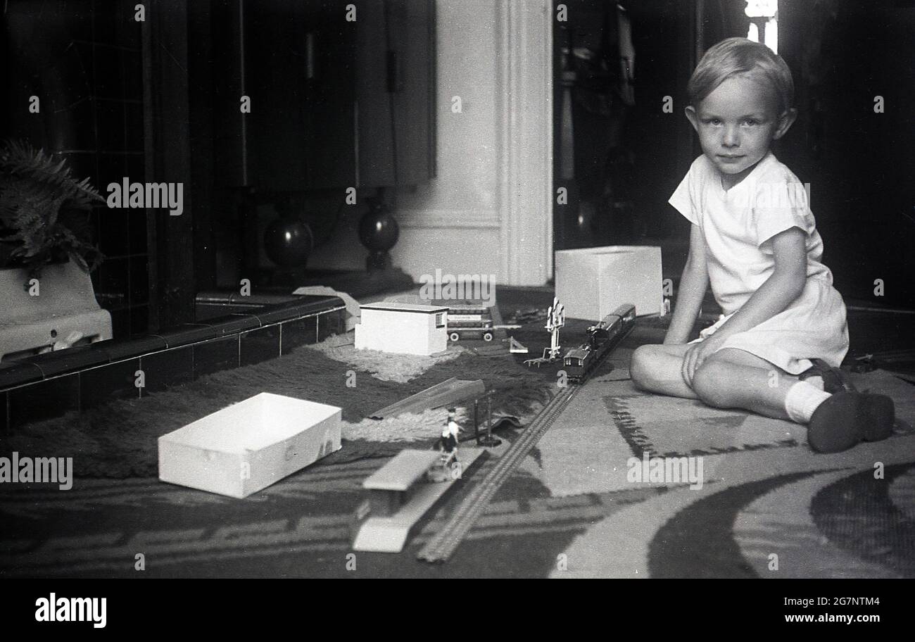 1950s, historical, young boy in a living room sitting on carpet infront of a fireplace with his train set, England, UK. Stock Photo