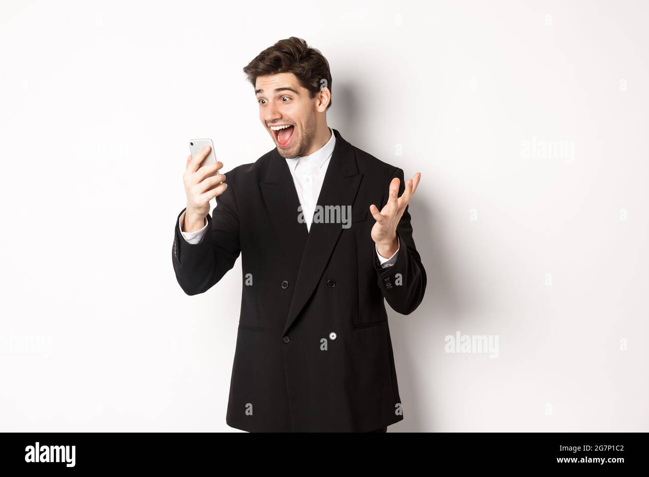 Portrait of happy smiling man in black suit, looking at smartphone ...