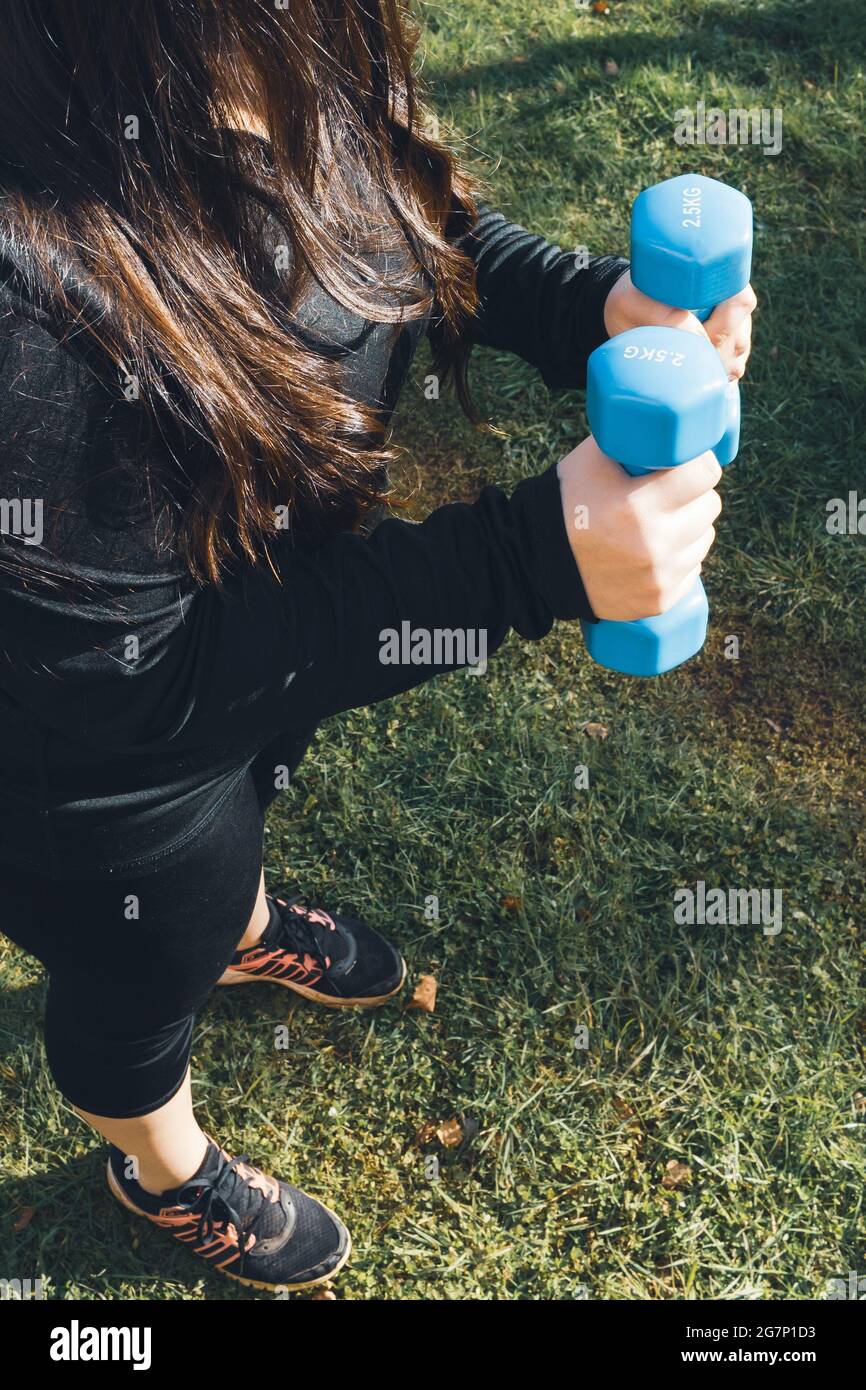 Plus size woman holding two blue dumbbells outdoor. Healthy life. Fitness concept Stock Photo