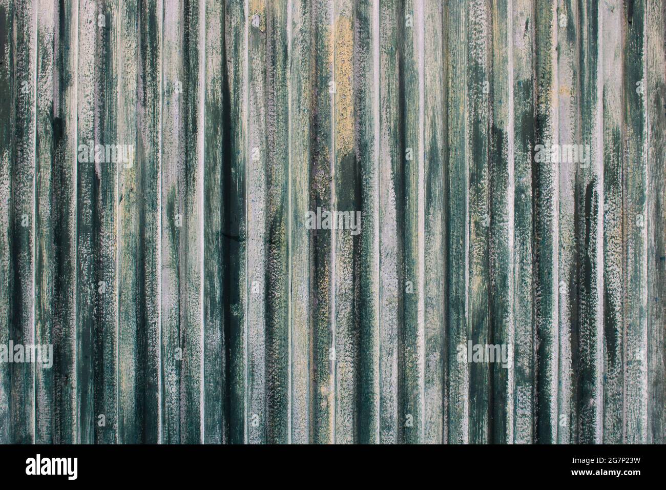 Texture of rusty metal surface with vertical stripes or slats and cracked paint in tones of green, white and yellow. Old weathered gate background Stock Photo