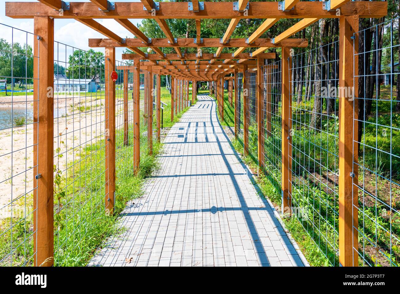 Wooden pergola (treillage) above cobblestone sidewalk leading along lake shoe and forest. One-point perspective. Stock Photo